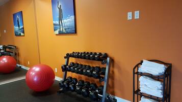 Un gimnasio con equipo de ejercicios, incluyendo pelotas rojas, un estante con mancuernas y toallas en un perchero.
