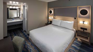 A hotel room with a large bed, a bathroom with a mirror and sink, and a chair.