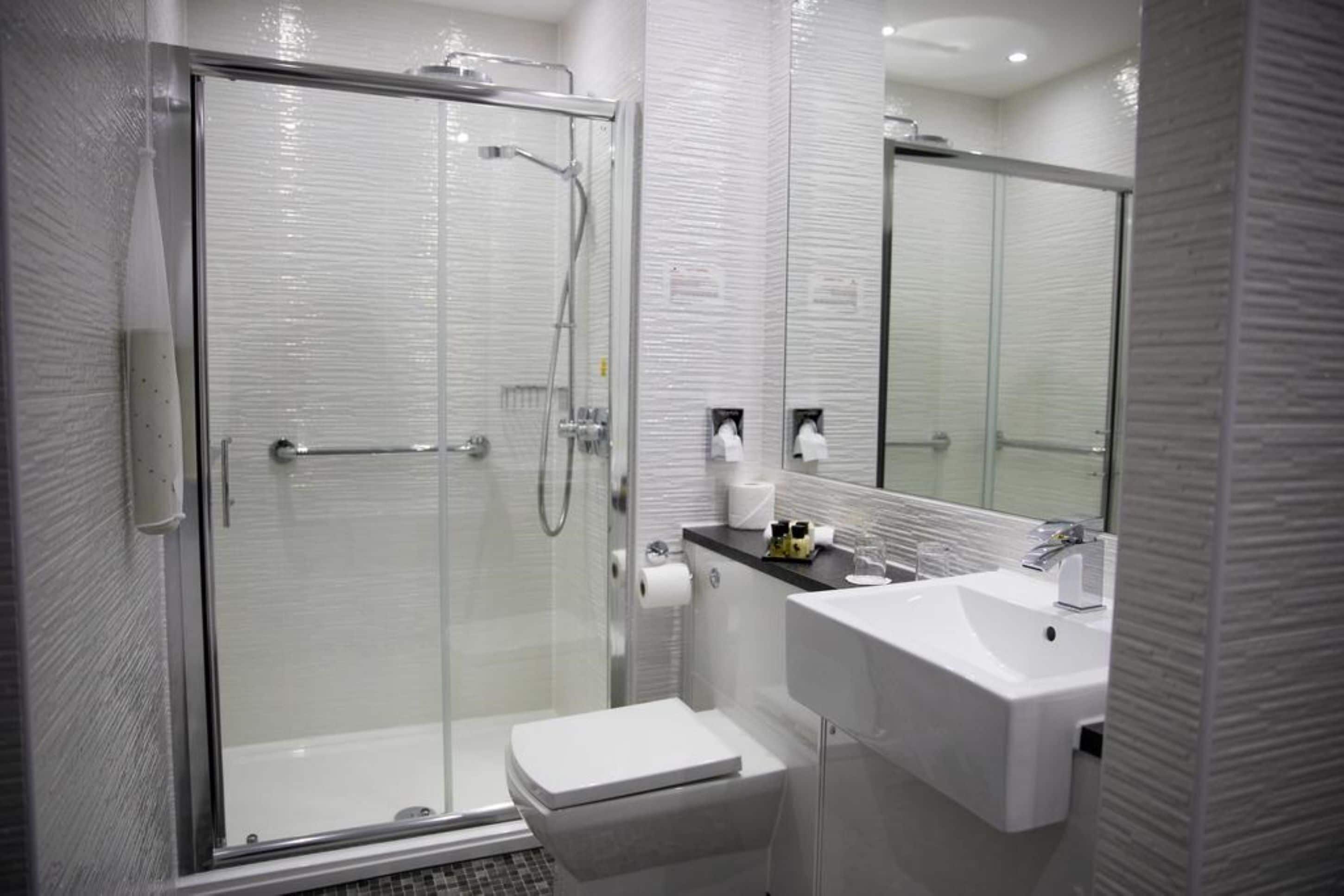 A modern bathroom with a glass-enclosed shower, a white toilet, and a sink with a mirror above it.