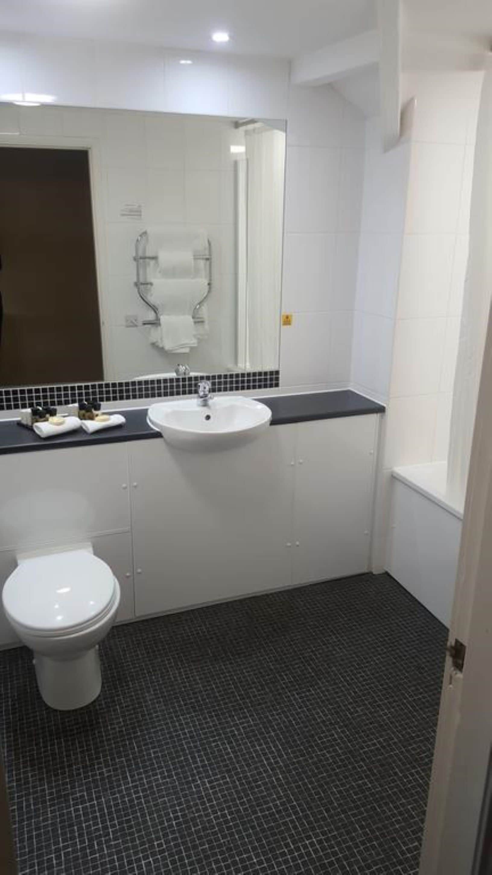 A bathroom with a white toilet, a sink with a black countertop, and a mirror above the sink.