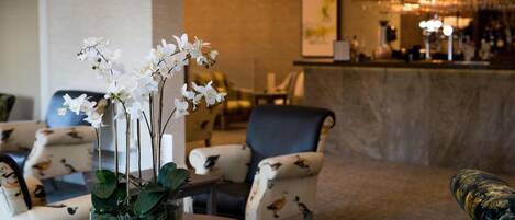 A lobby area with a round table, a vase with white flowers, and a bar counter in the background.