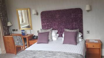 Une chambre d’hôtel avec un grand lit, deux tables de chevet, un bureau avec une chaise, un miroir et une lampe.