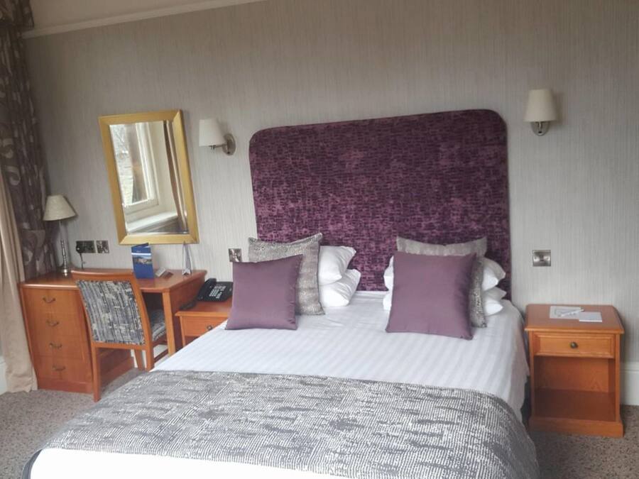 Une chambre d’hôtel avec un grand lit, deux tables de chevet, un bureau avec une chaise, un miroir et une lampe.