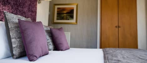 A neatly made bed with a patterned headboard and pillows, a framed picture on the wall, and a wooden wardrobe.