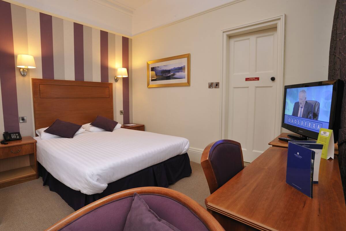 A hotel room with a large bed, bedside lamps, a television, a desk, and a chair.