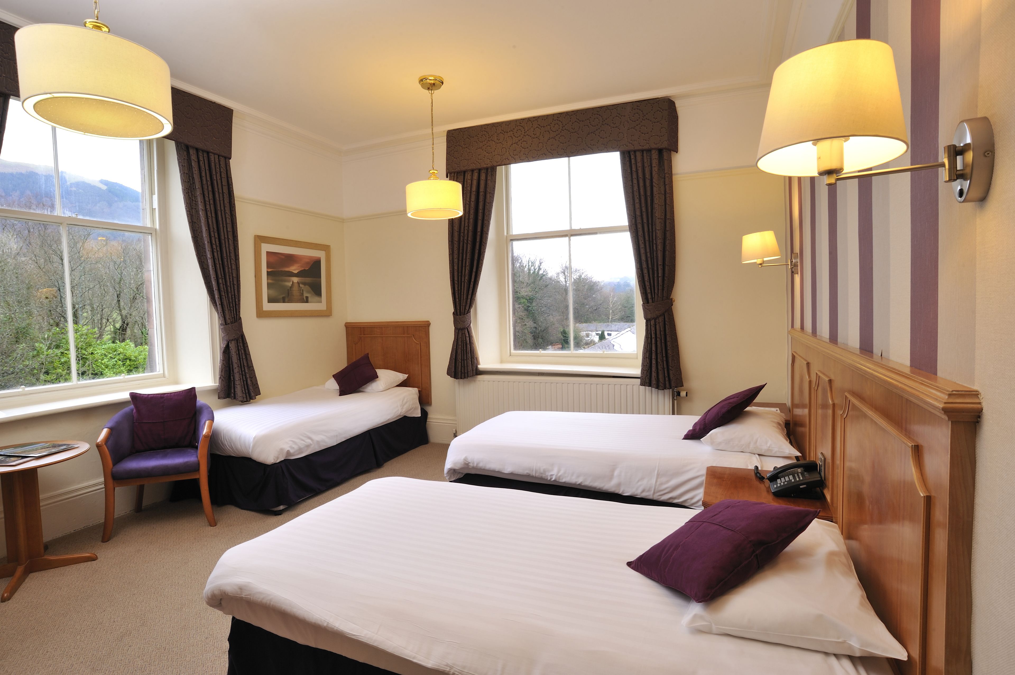 A hotel room with two beds, a chair, a table, and a view of the outdoors.
