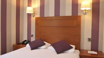 Habitación de hotel con una cama grande, dos mesitas de noche, un cabecero de madera y dos lámparas de pared.