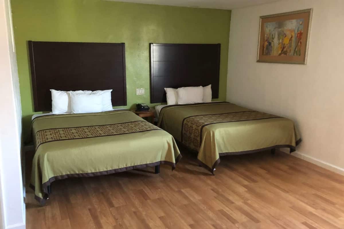 Ein Hotelzimmer mit zwei Betten, grünen Wänden, Holzboden und einem Bild an der Wand.