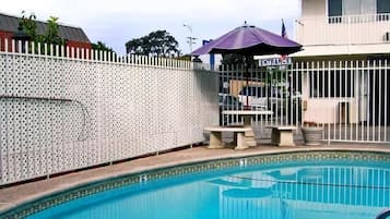 A swimming pool with a white fence, a covered seating area, and a building with an entrance sign.