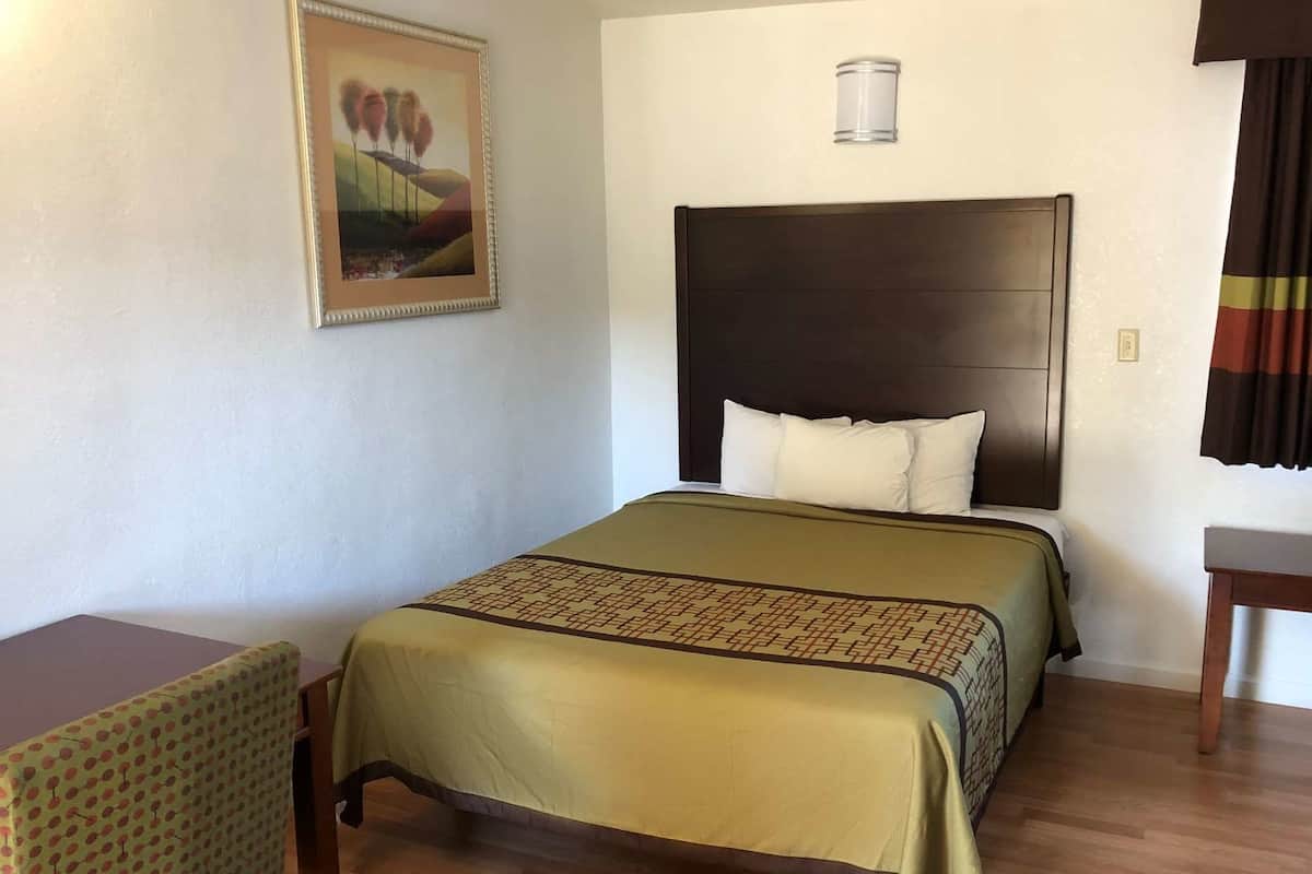 Ein Hotelzimmer mit Bett, Sessel, einem Bild an der Wand und einem Nachttisch.
