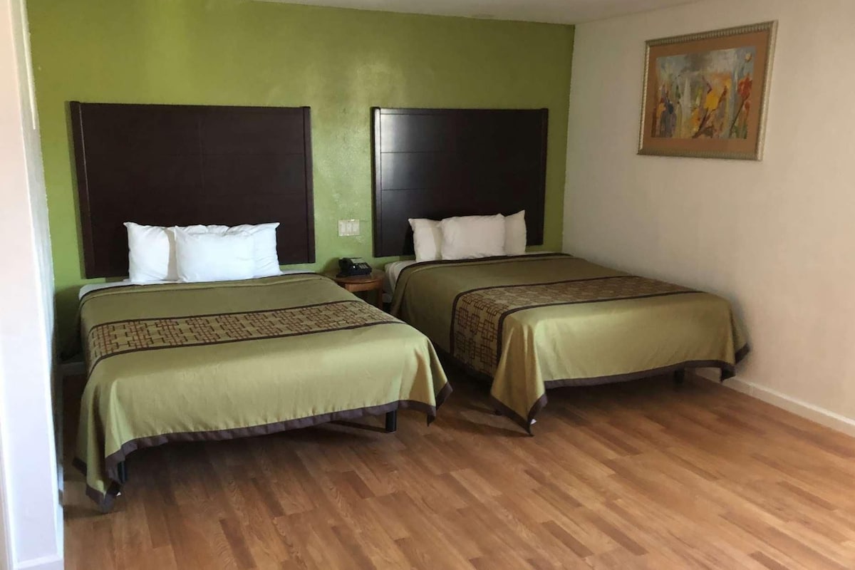 A room with two beds, green walls, wooden flooring, and a painting on the wall.