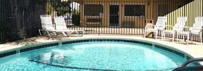 A swimming pool with lounge chairs, a wooden fence, and a building with windows and a door. - Americas Best Value Inn Visalia (Visalia)