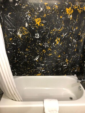 A bathtub with a white towel, set against a black and yellow marble wall. - Americas Best Value Inn Visalia (Visalia)