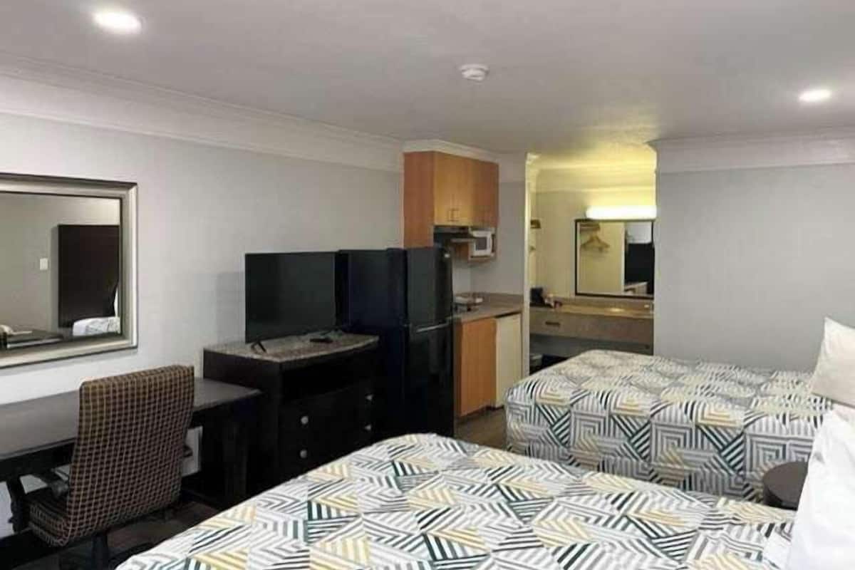 A hotel room with two beds, a desk, a chair, a television, a microwave, and a small kitchenette.