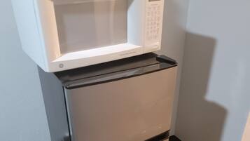 A compact refrigerator with a built-in microwave on top, positioned against a wall with a wooden floor.