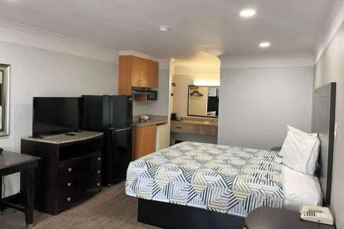 A hotel room with a bed, a desk, a television, a small kitchenette, and a bathroom.