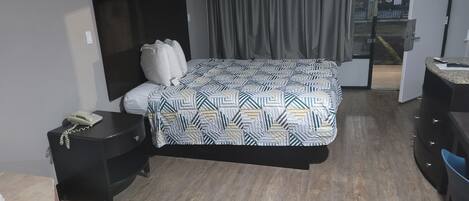 A hotel room with a bed, a desk, a chair, a telephone, and a curtain.