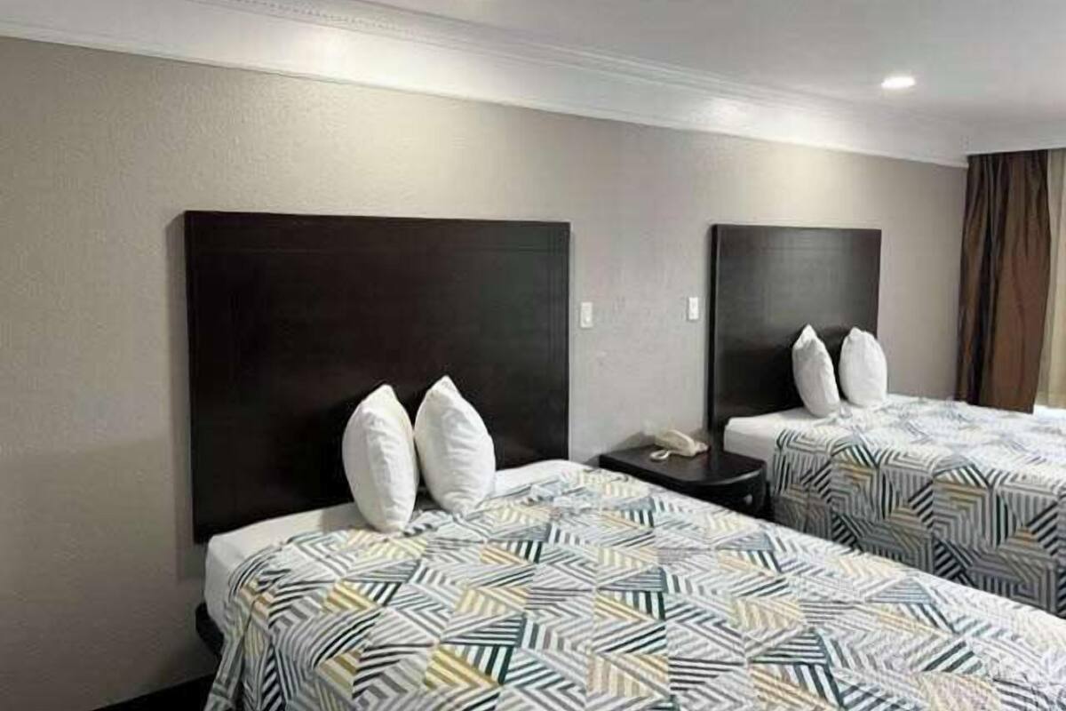 A hotel room with two beds, each with a dark headboard and white pillows. The beds have patterned bedding.
