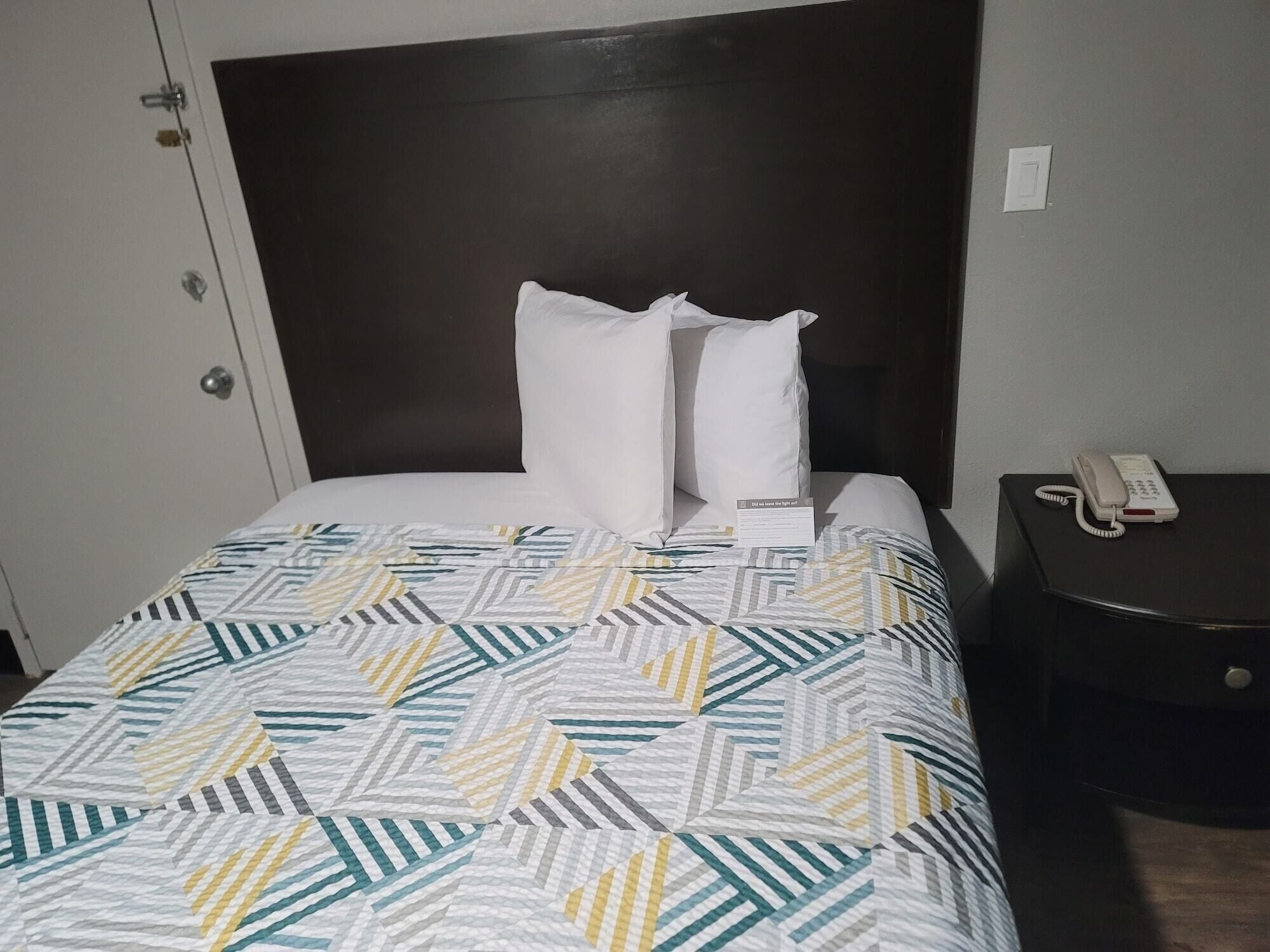 A neatly made bed with a patterned bedspread, a dark headboard, and a bedside table with a telephone.