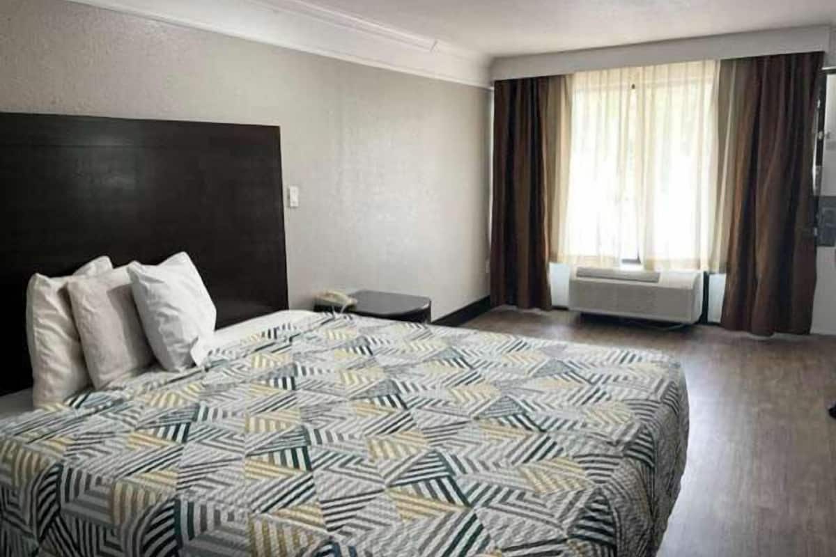 A hotel room with a large bed, a dark headboard, a bedside table, and a window with curtains.