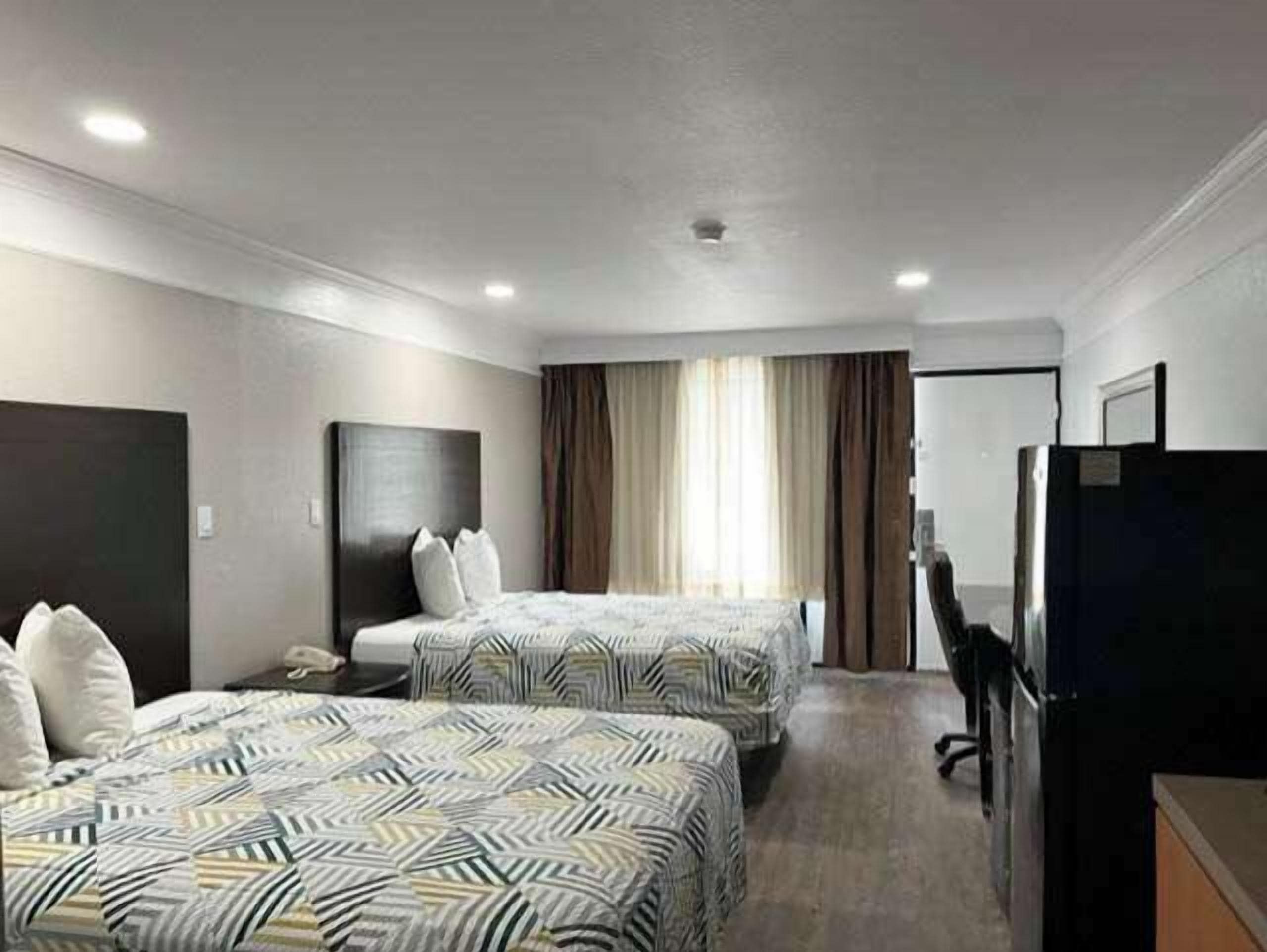 A hotel room with two beds, a desk, a television, and a window with curtains.