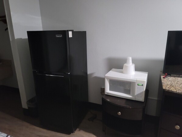 Un refrigerador negro y un microondas blanco sobre una encimera oscura en una cocina.
