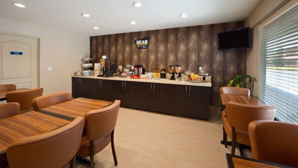 A hotel reception area with a counter, seating, and a television. - Studio 6 Suites Hinesville, GA  (Hinesville)