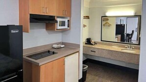 A compact kitchen with wooden cabinets, a microwave, a coffee maker, and a sink. - Studio 6 Suites Hinesville, GA  (Hinesville)