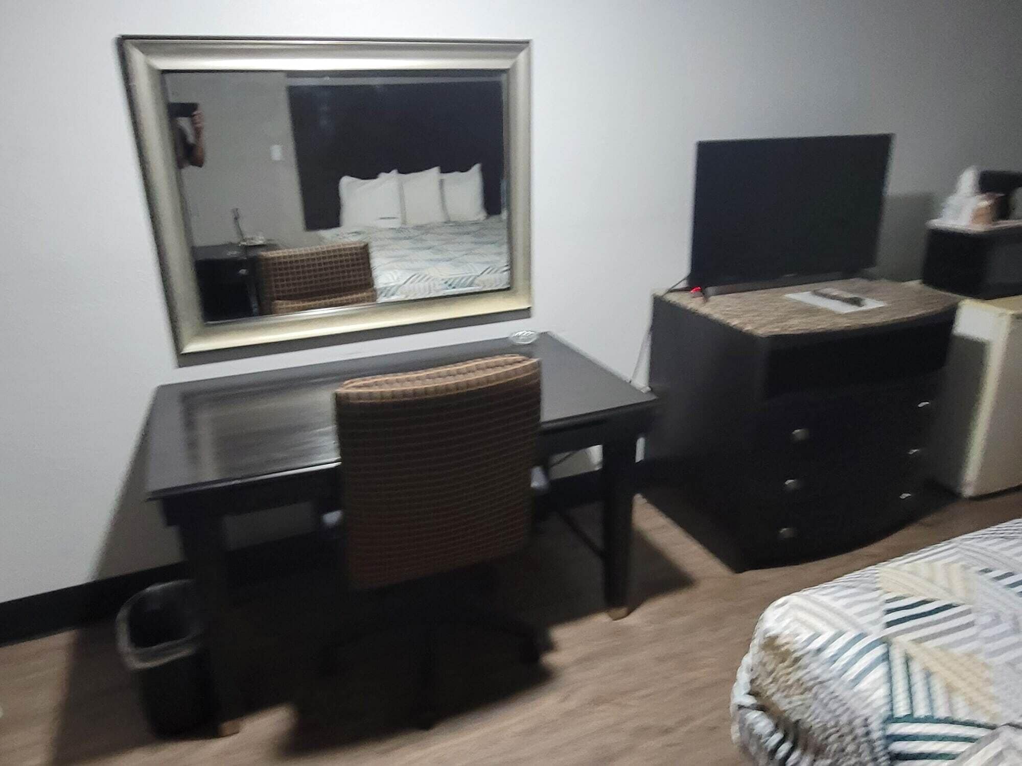 A hotel room with a large mirror, a desk, a chair, a television, a dresser, and a bed.