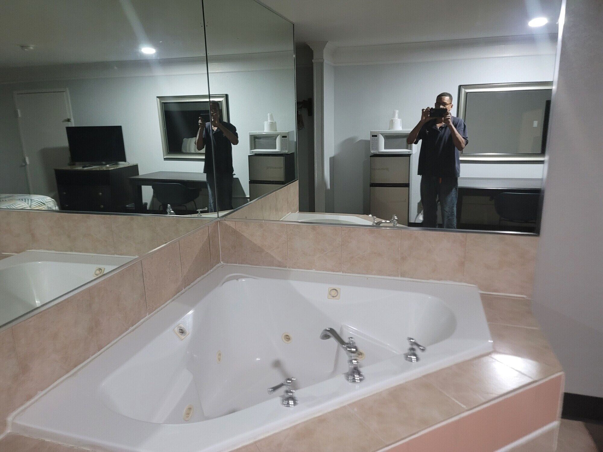 A bathroom with a large bathtub, a mirror, a sink, and a microwave.
