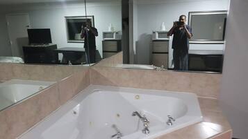 A bathroom with a large bathtub, a mirror, a sink, and a microwave.