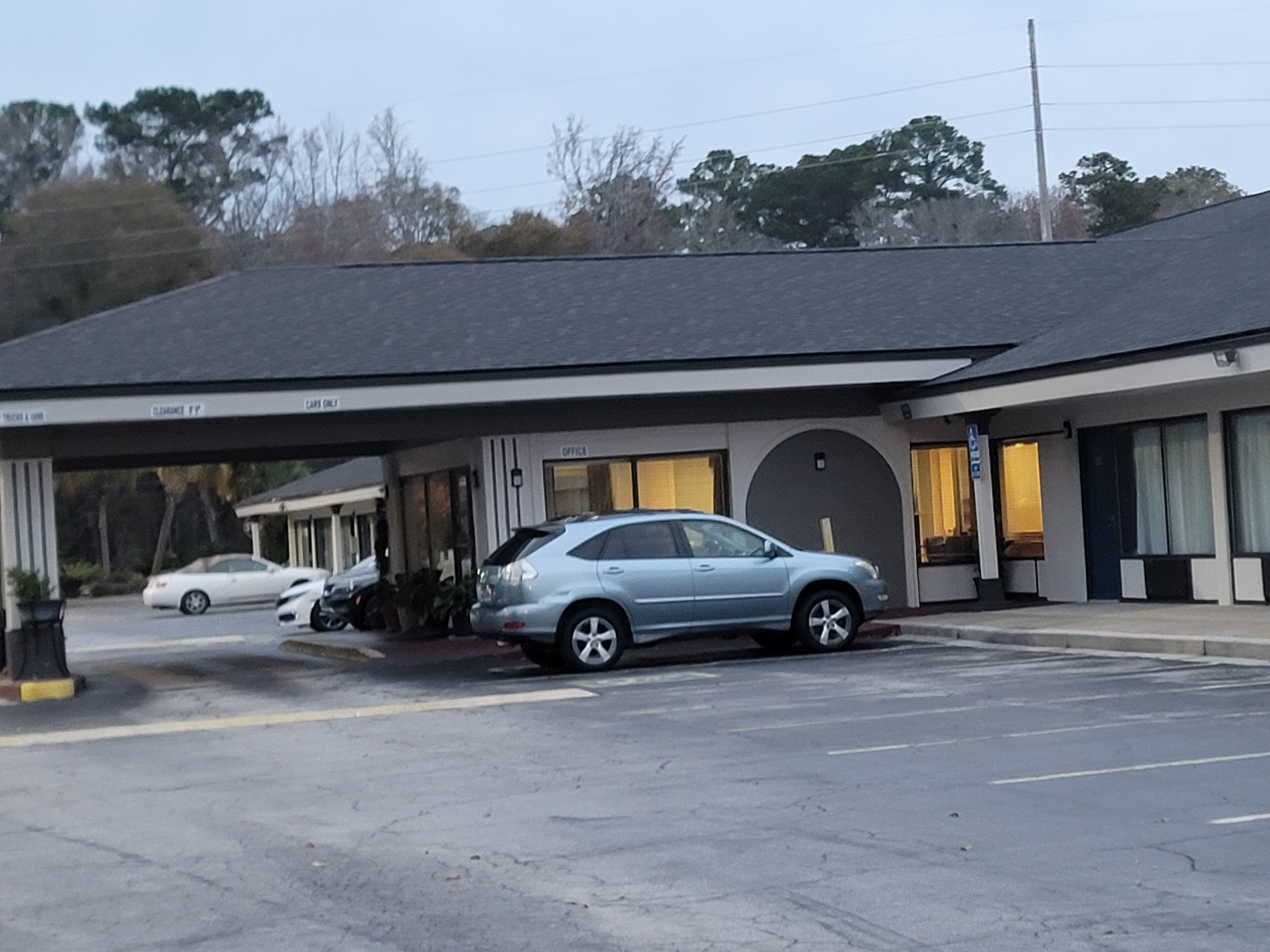 A building with a covered parking area, a car, and a white car parked outside.