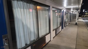 A row of train car windows with curtains, a concrete platform, and a building facade with signage. - Studio 6 Suites Hinesville, GA  (Hinesville)