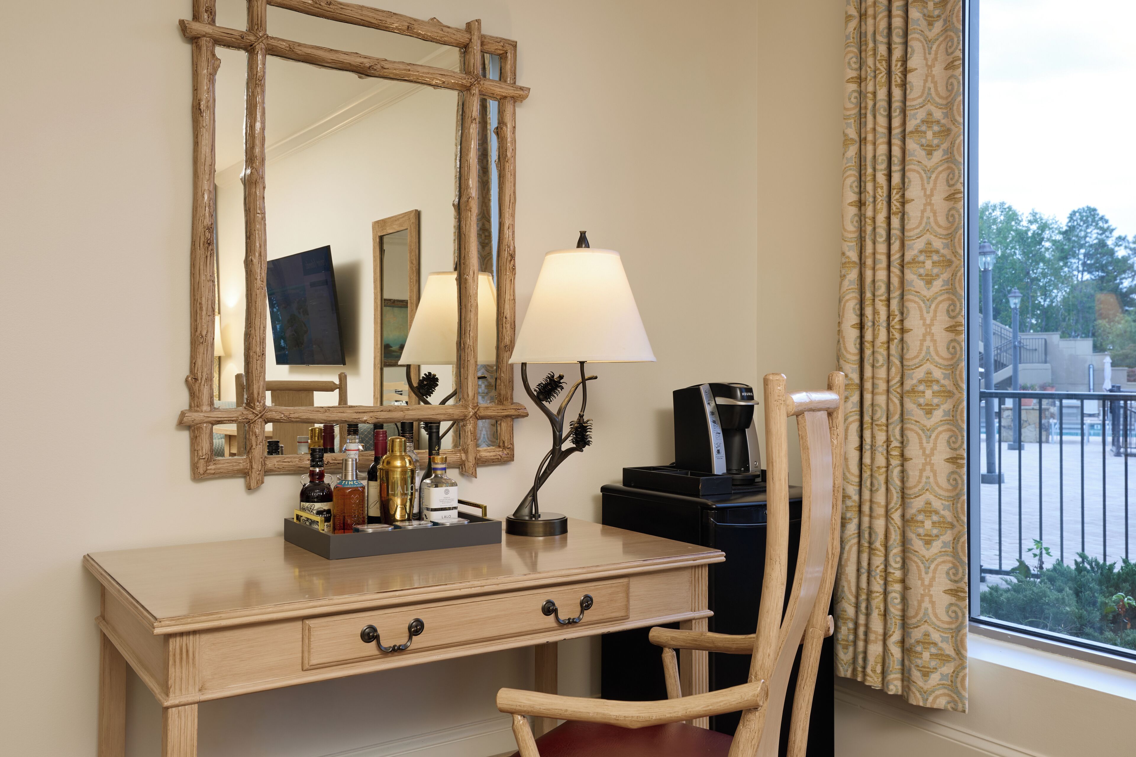 A hotel room with a wooden desk, a mirror, a lamp, and a chair.