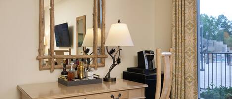 A hotel room with a wooden desk, a mirror, a lamp, and a chair.