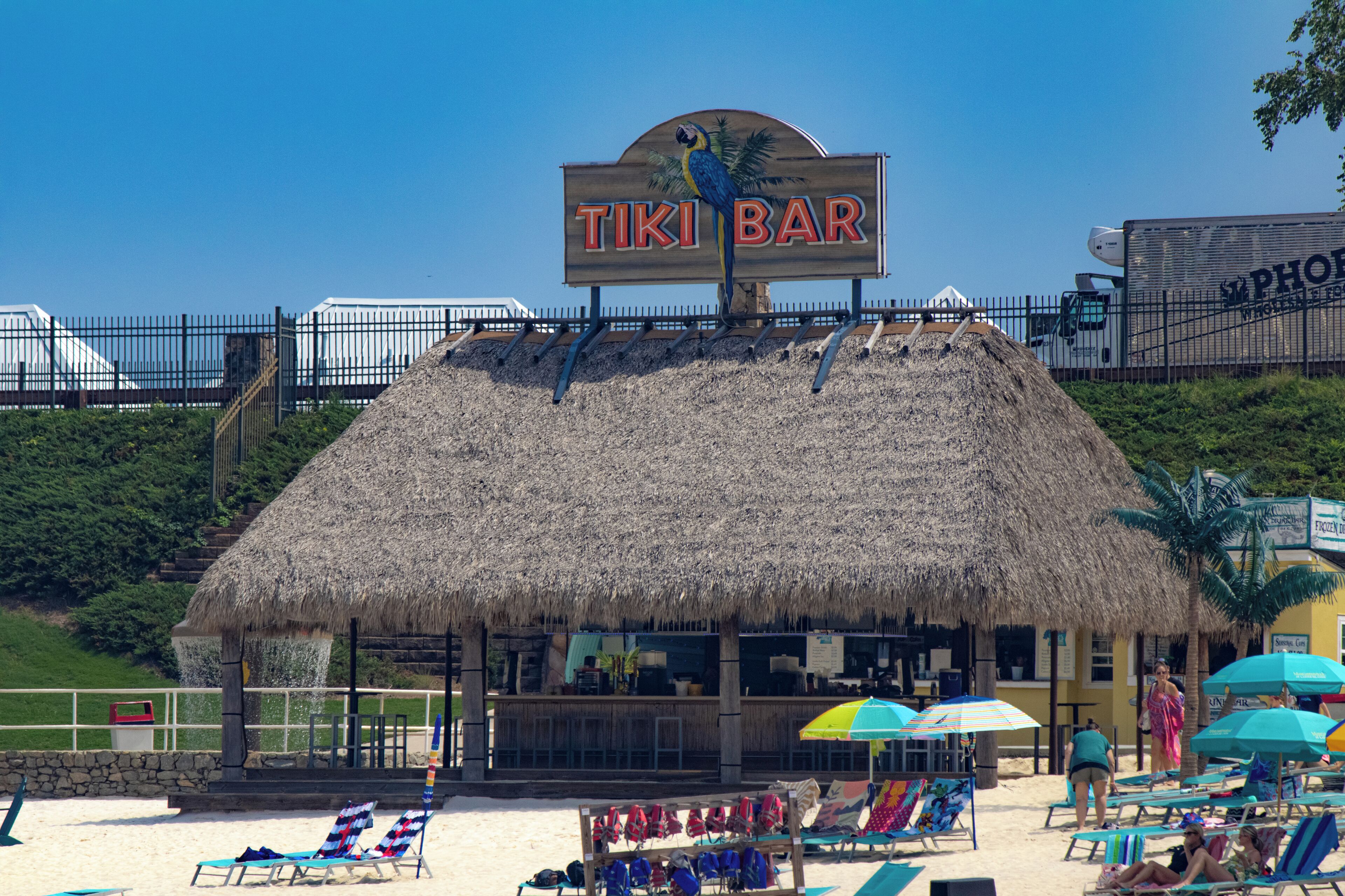 Un bar de plage appelé TIKI BAR, doté d’un toit de chaume, de chaises longues et de parasols.