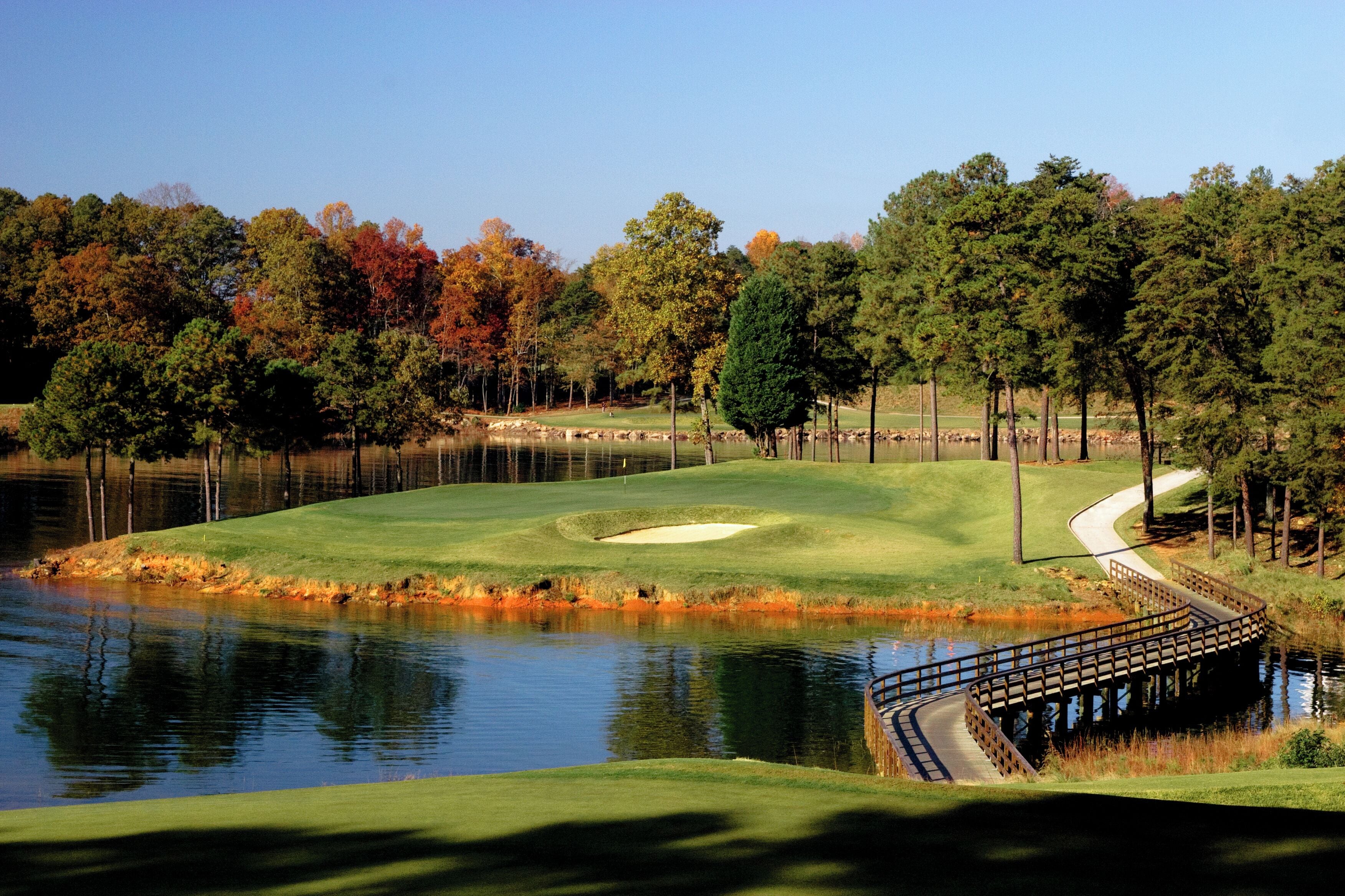 A golf course with a pond, trees, and a wooden bridge.