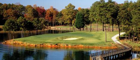 A golf course with a pond, trees, and a wooden bridge.