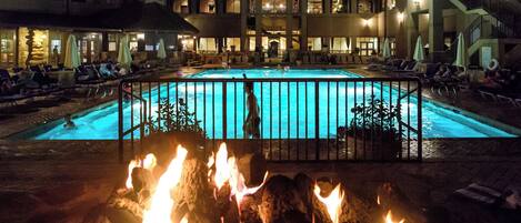 A hotel with a swimming pool, lounge chairs, and a fire pit area.