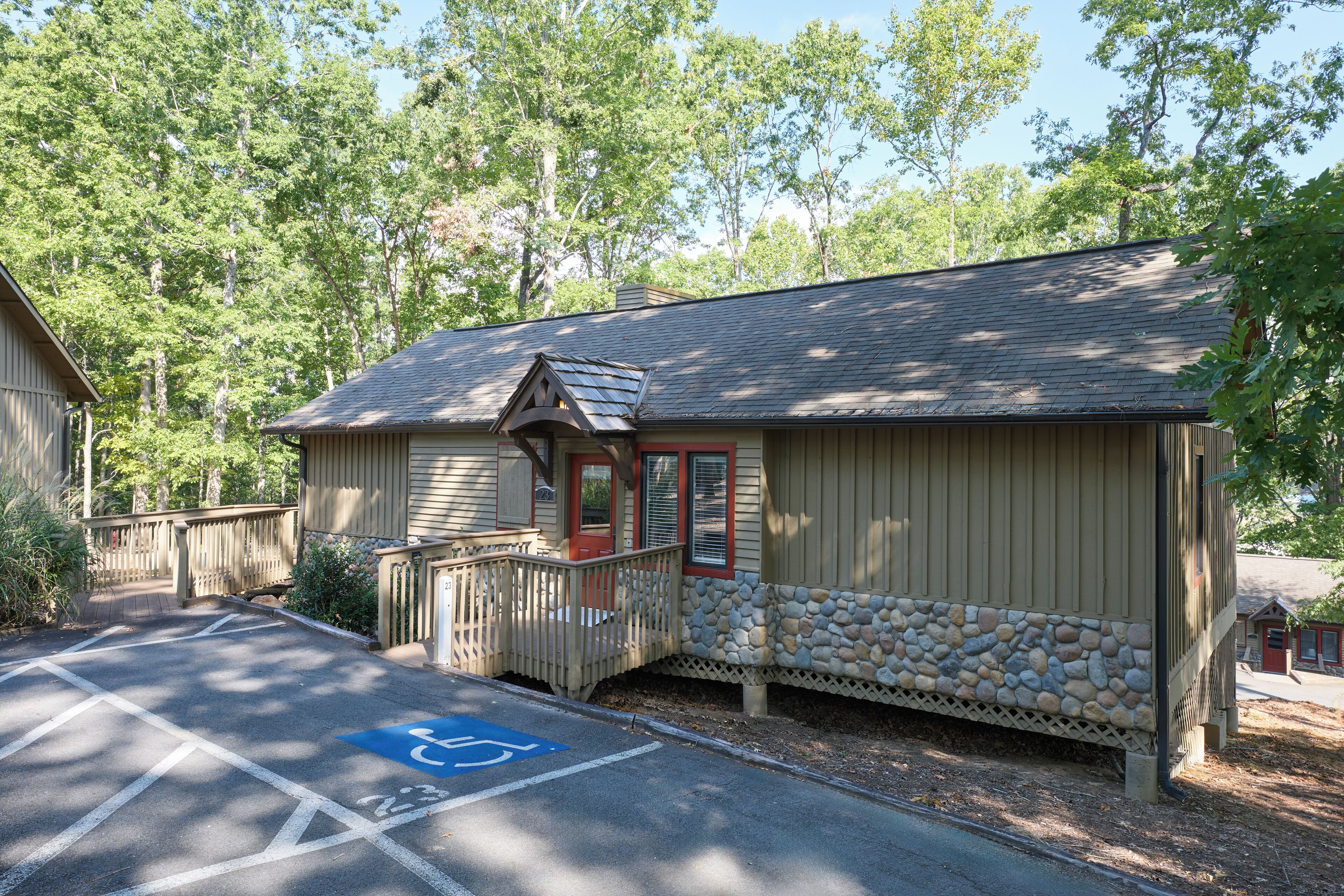 A building with a stone base and a wooden upper section, a wheelchair-accessible parking space, and a small porch with a railing.