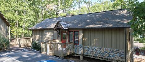 A building with a stone base and a wooden upper section, a wheelchair-accessible parking space, and a small porch with a railing.