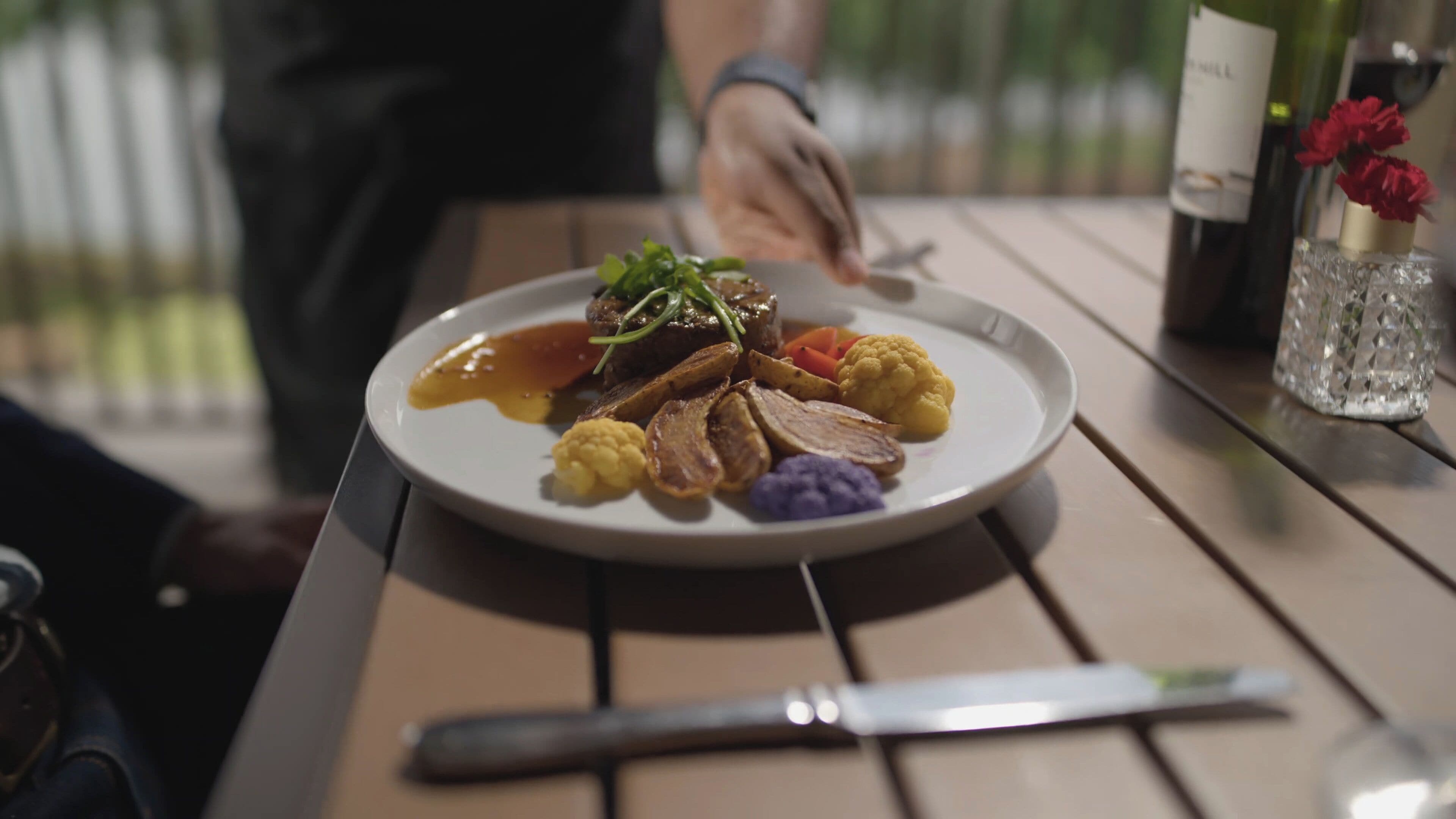 A plate of food on a wooden table with a knife and a bottle of wine in the background.