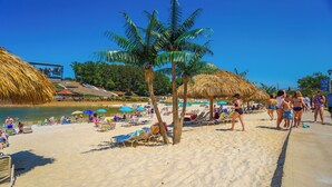 A beach with palm trees, umbrellas, and lounge chairs. - Lanier Islands Resort (Buford)