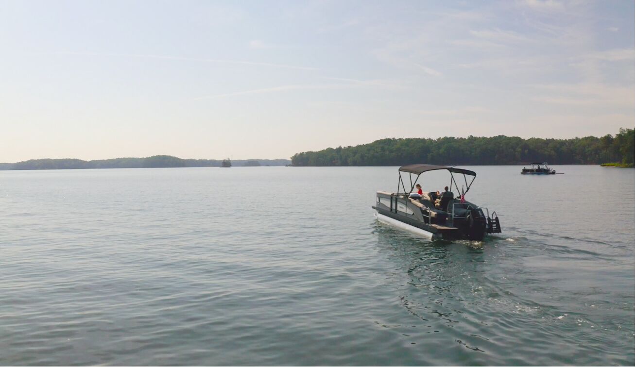 Ein Boot auf einem ruhigen See mit bewaldeter Uferlinie im Hintergrund.