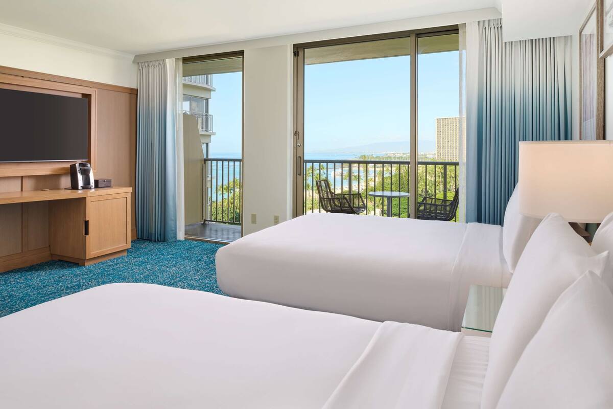 A hotel room with two beds, a TV, a coffee maker, and a balcony with a view of the city.