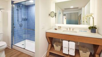 A bathroom with a glass-enclosed shower, a white sink with a mirror, and wooden shelves with baskets.