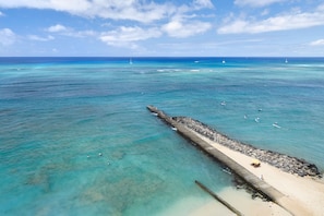 A coastal scene with clear turquoise waters, a sandy beach, and a rocky breakwater.