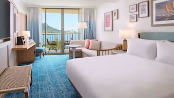 Habitación de hotel con cama, escritorio con silla, pequeña mesa con silla y balcón con vista a las montañas.