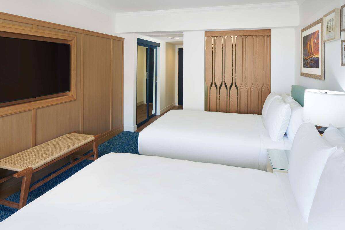 A hotel room with two beds, a TV, a bench, a mirror, and a wardrobe.