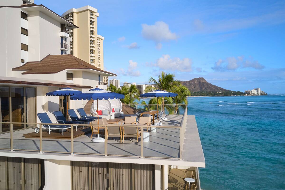 A deck with lounge chairs and umbrellas, overlooking a body of water and a mountain.